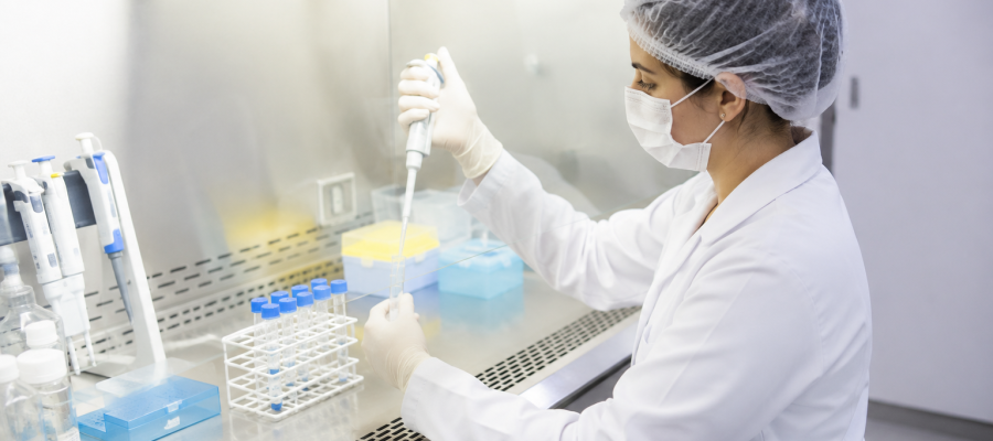Técnico de laboratório manipulando amostras estéreis em capela de fluxo laminar.